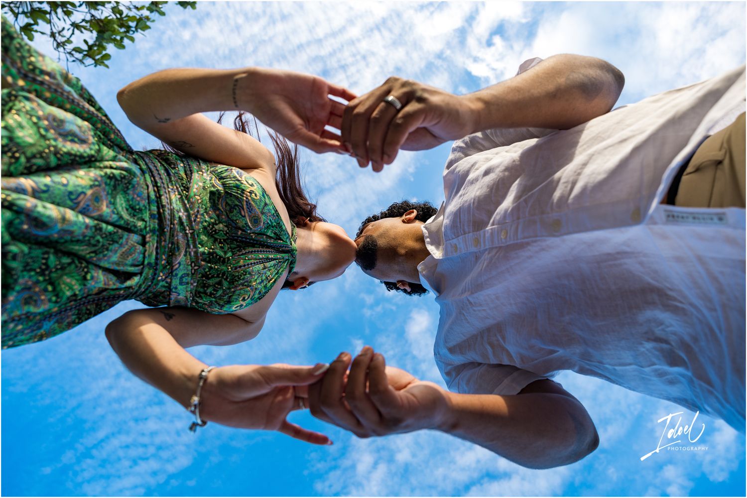 Two people hold hands against a bright blue sky with wispy clouds in a unique low-angle perspective shot.