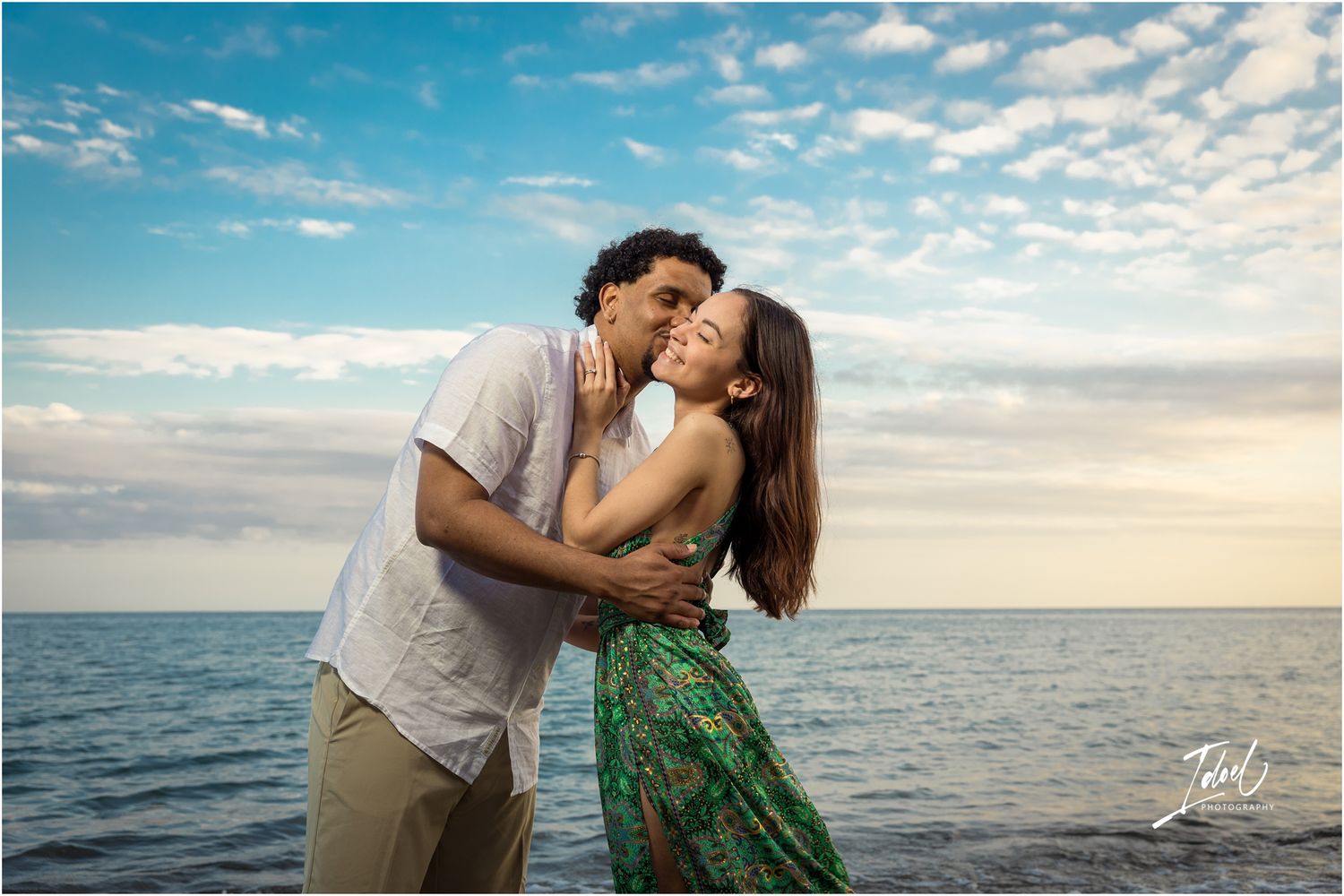 An intimate couple shares a tender moment on the shoreline as golden sunlight reflects off the ocean.
