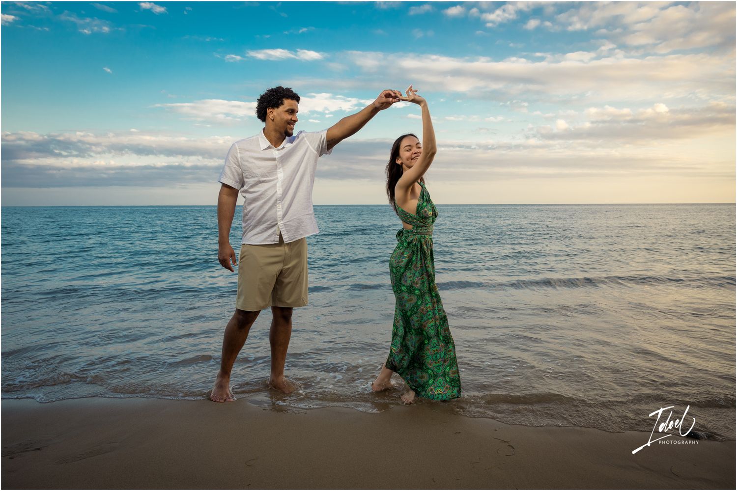 A romantic couple dances together at sunset on the beach with ocean waves and golden light in the background.