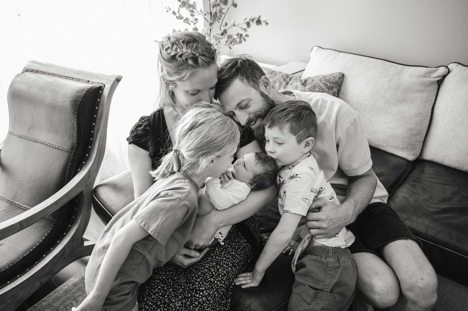 Black and white photo of family cuddling together on couch during lifestyle session.