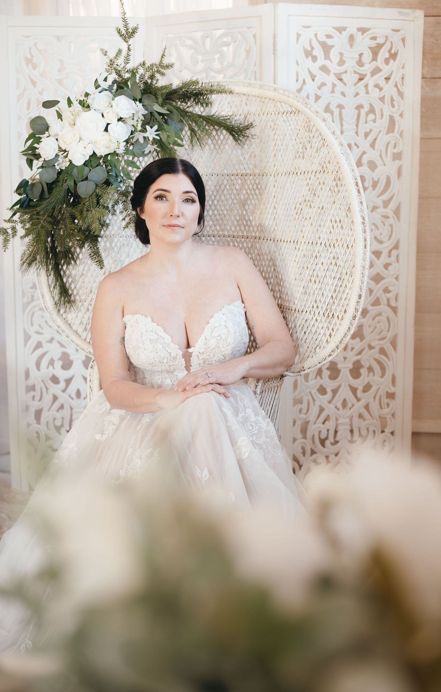Bridal portrait session with peacock chair and white decorative backdrop adorned with greenery.