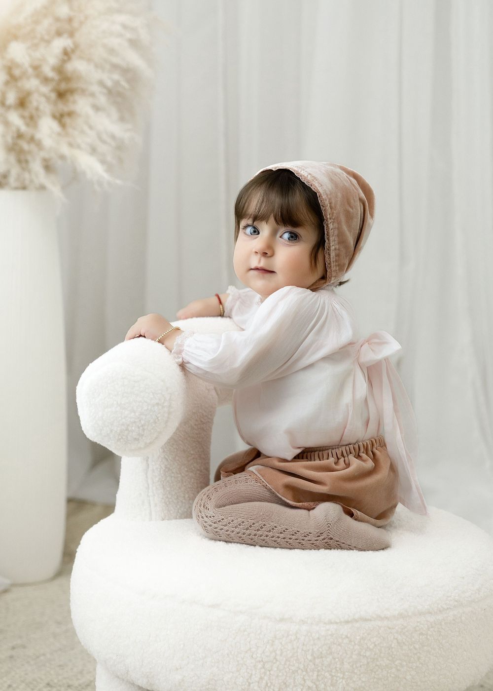 A person in soft neutral tones reclines on a white curved surface with pampas grass decor in the background.