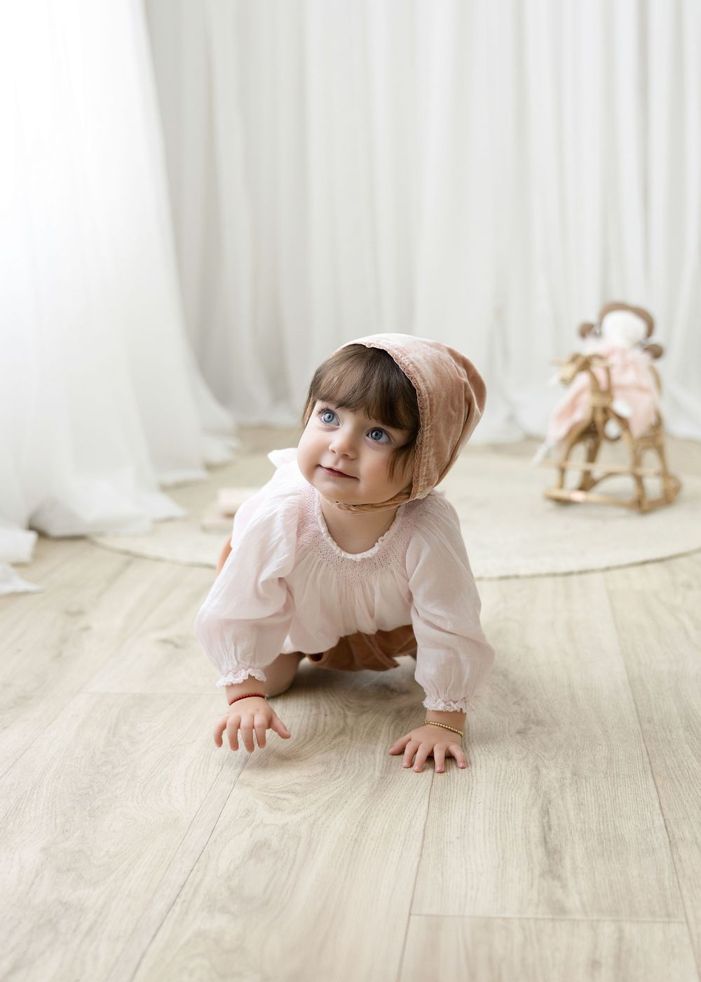 Child in pink crawling and playing on wooden floor in bright white room with natural light.