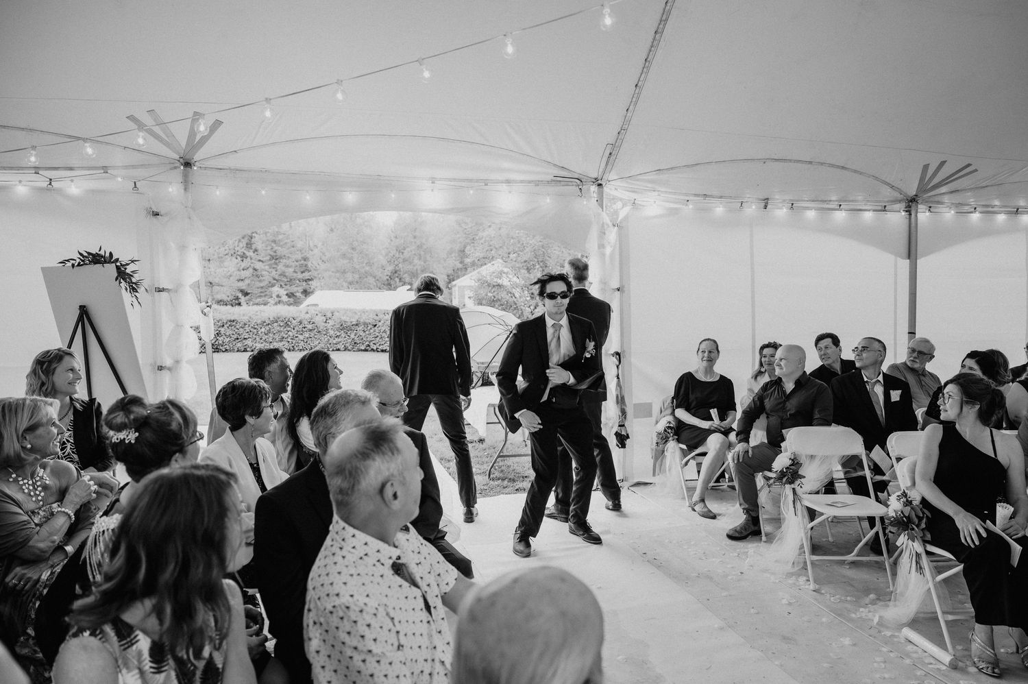 Wedding guests gather under a white tent decorated with string lights during an intimate celebration.