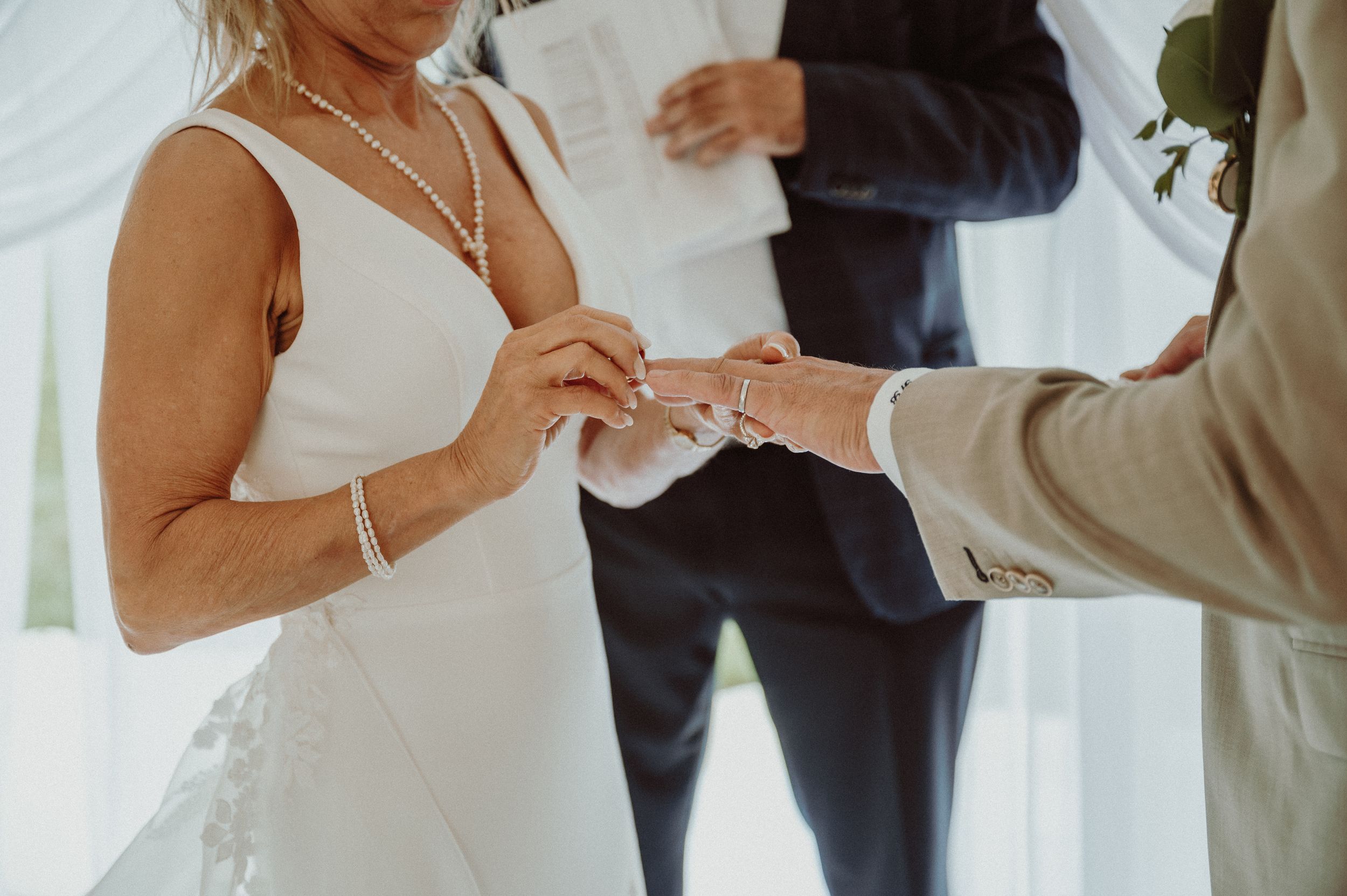 Close-up of couple exchanging rings during wedding ceremony under white tent.