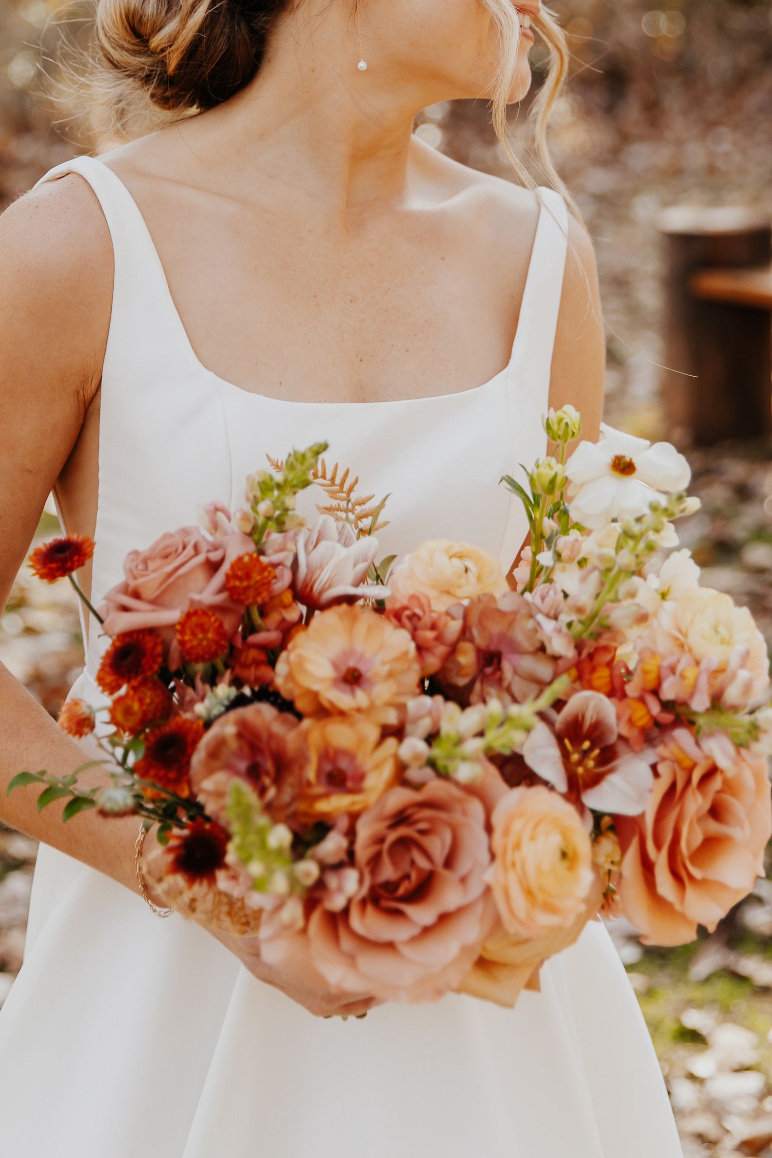 Close-up of peach and coral bridal bouquet with roses and mixed flowers against white wedding dress.