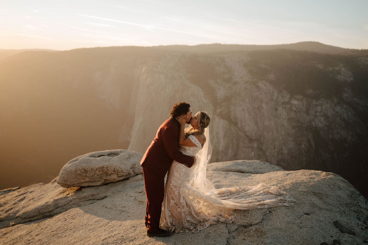 Couple sharing a dramatic kiss on a cliff at Yosemite during golden sunset.