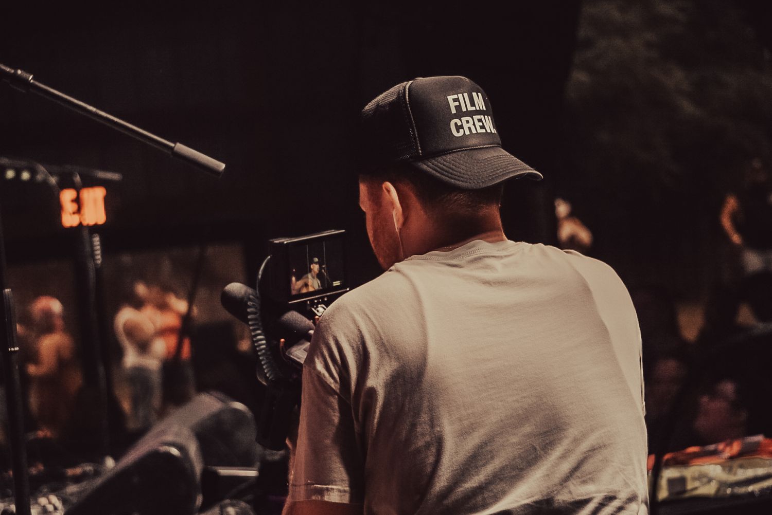 Camera operator filming at event wearing baseball cap.