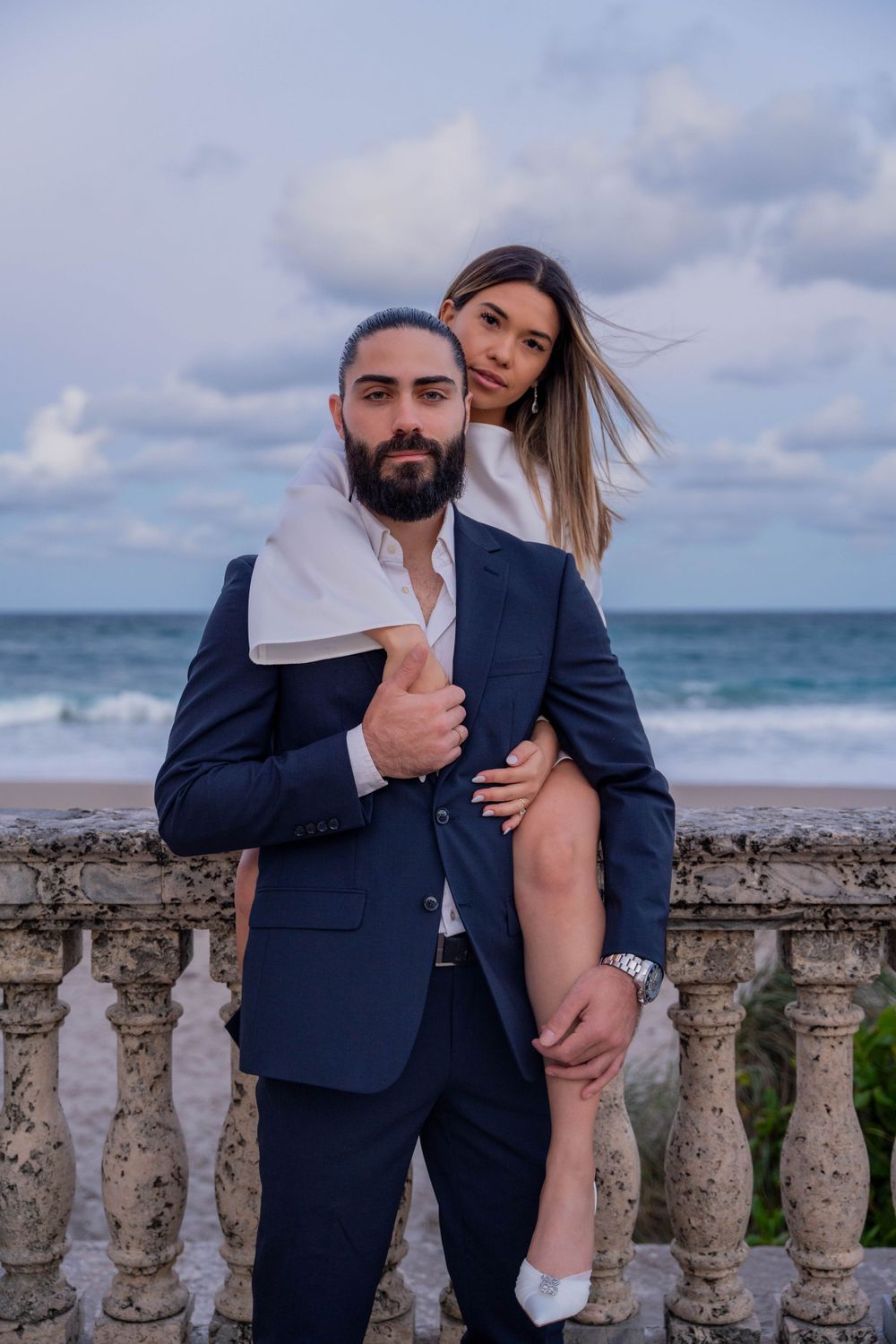 Stylish couple poses by the ocean in elegant attire. Sophisticated engagement photography with a modern, editorial aesthetic. Worth Avenue