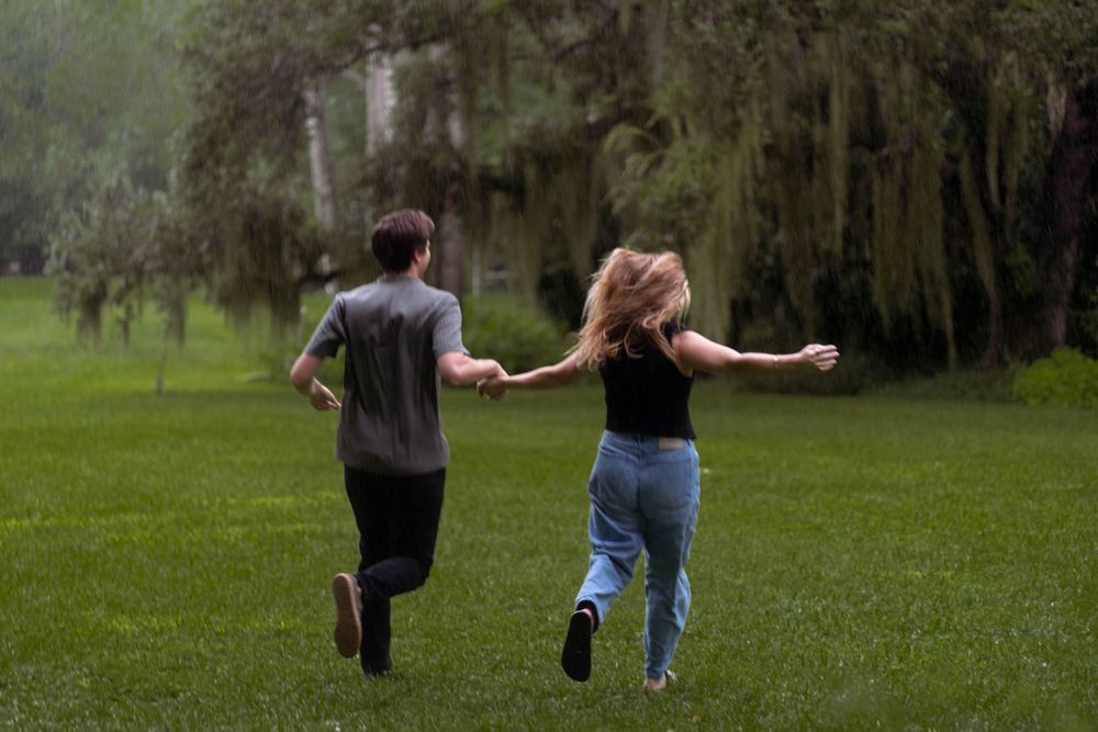 Couple running hand-in-hand through the rain, celebrating love. Candid engagement photography with a whimsical, romantic feel.