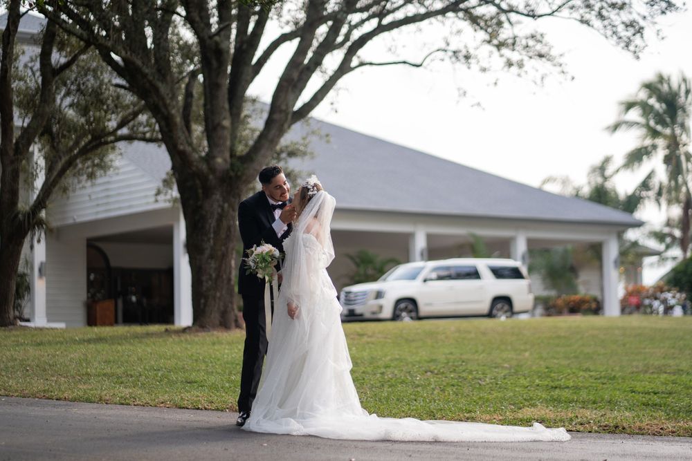 Groom lifts bride’s veil as they smile outdoors. Candid wedding photography capturing love, joy, and timeless romance.