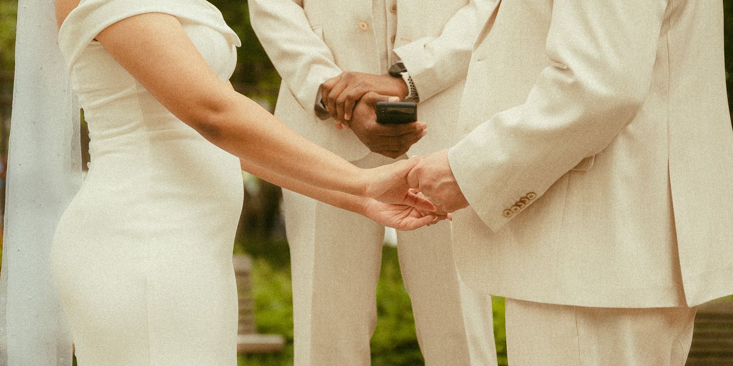 Bride and groom holding hands during outdoor wedding ceremony with officiant in white suit.