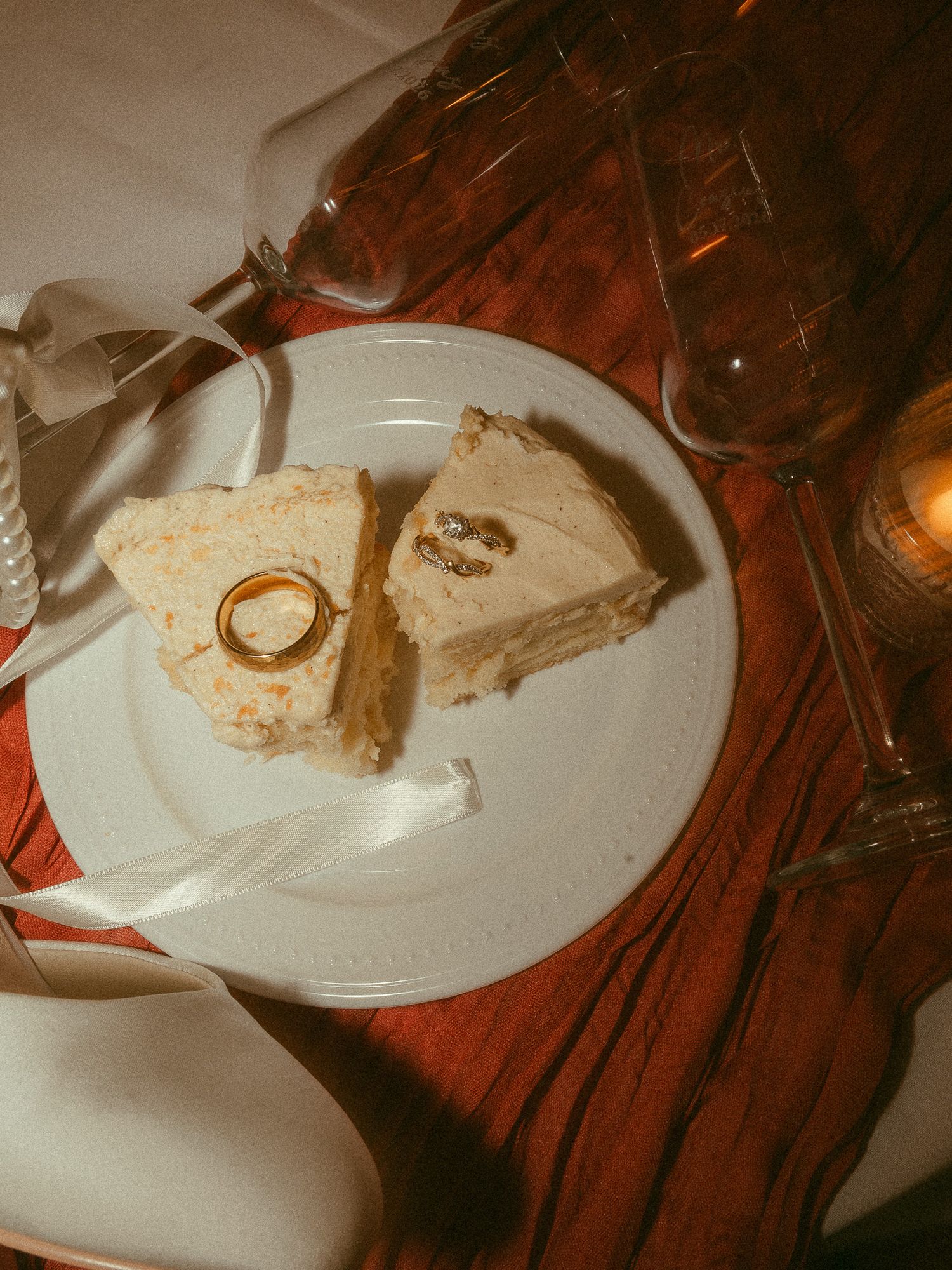 Wedding rings resting on a slice of white cake on a decorative plate with champagne glasses nearby.