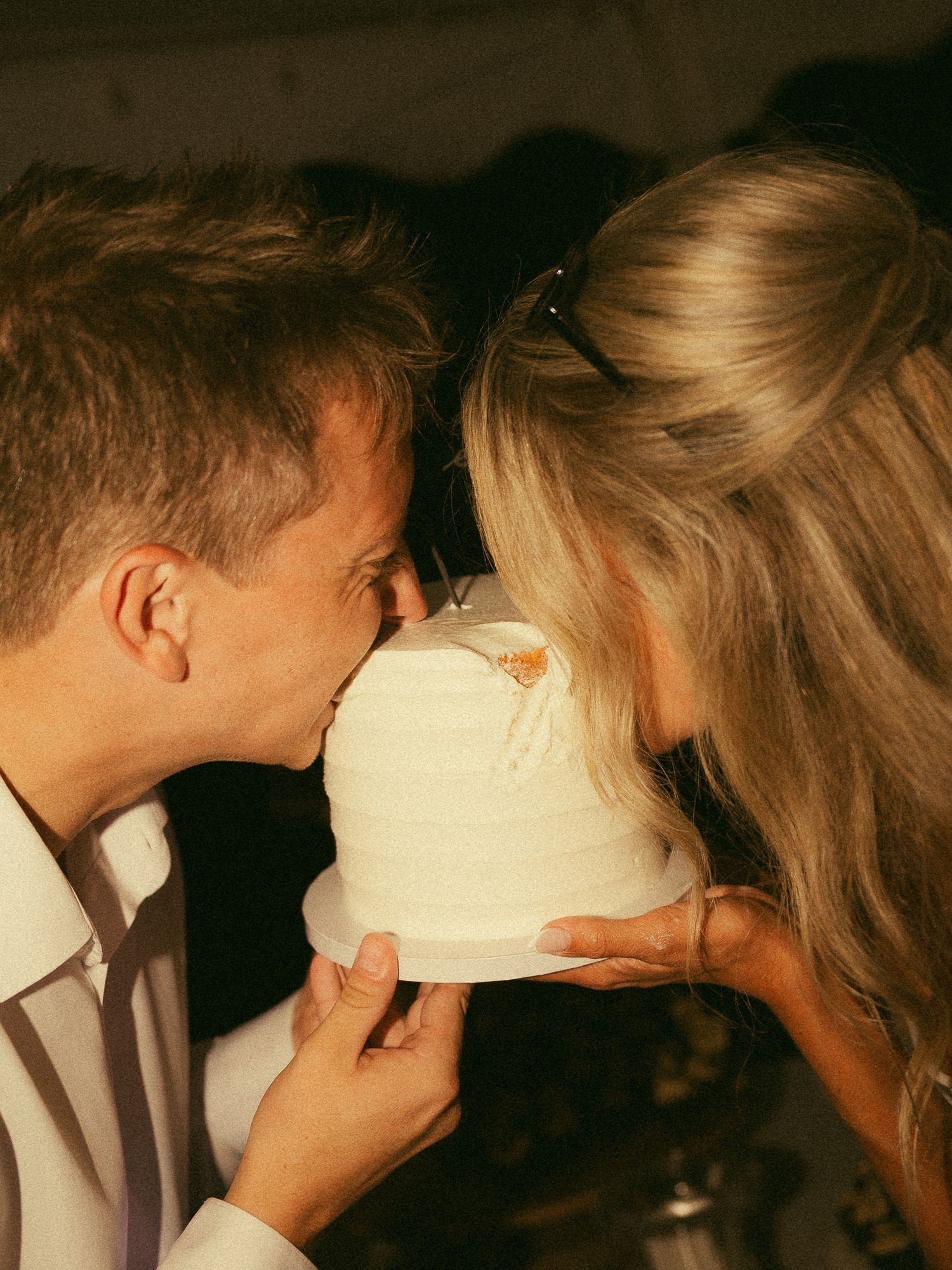 Couple sharing a romantic bite of white wedding cake together at their reception celebration.
