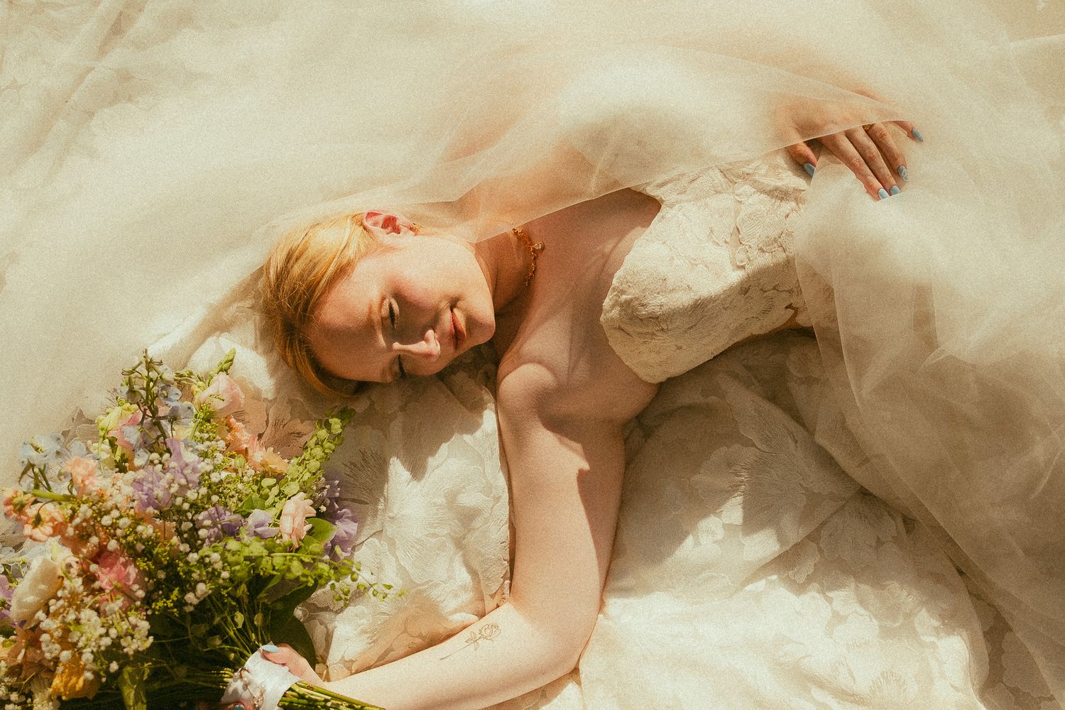 A bride in a flowing lace wedding gown lies gracefully on the floor holding a colorful wildflower bouquet.