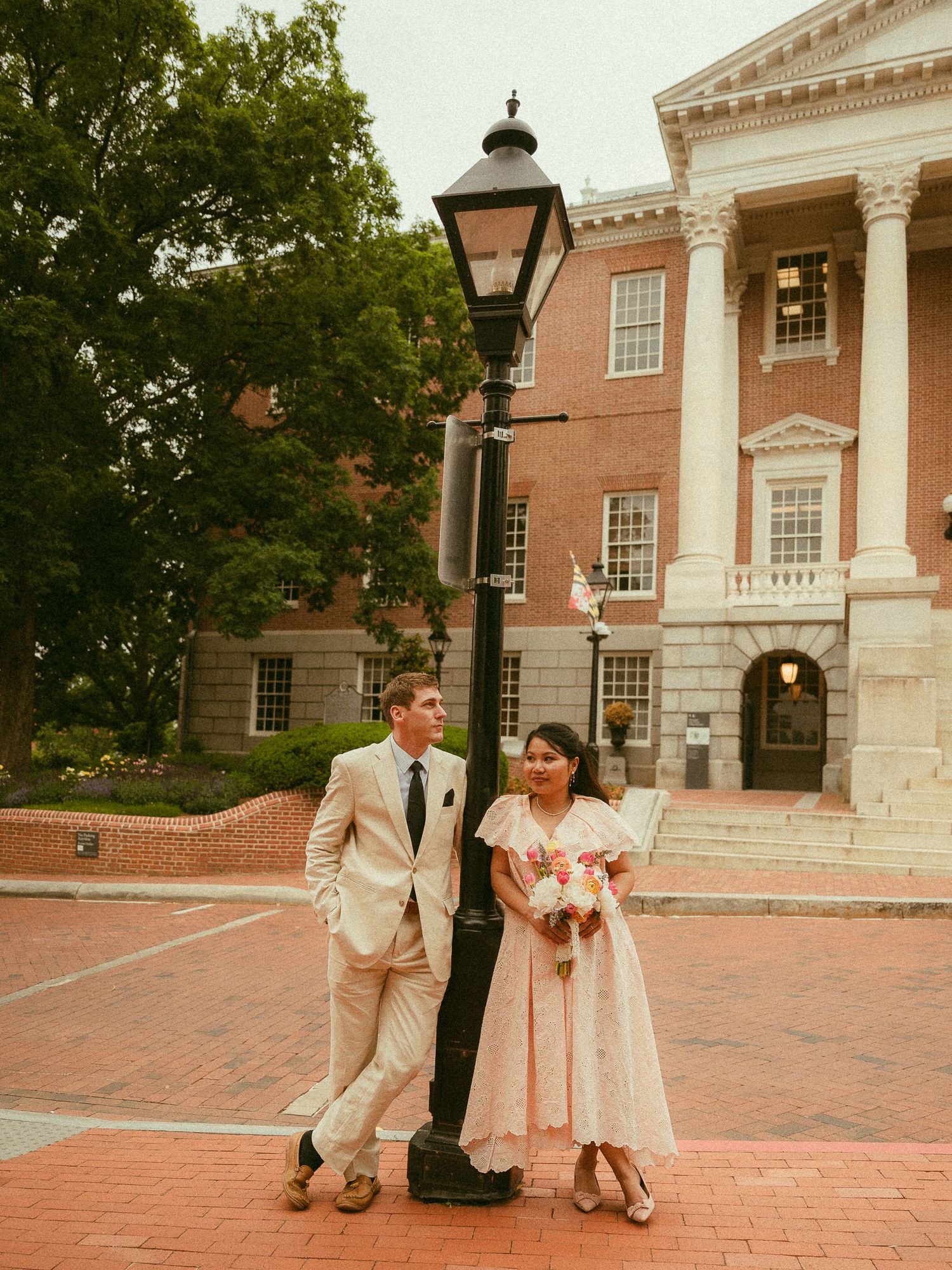 Bride and groom posing by a lamp post in front of a classic brick building on their wedding day.