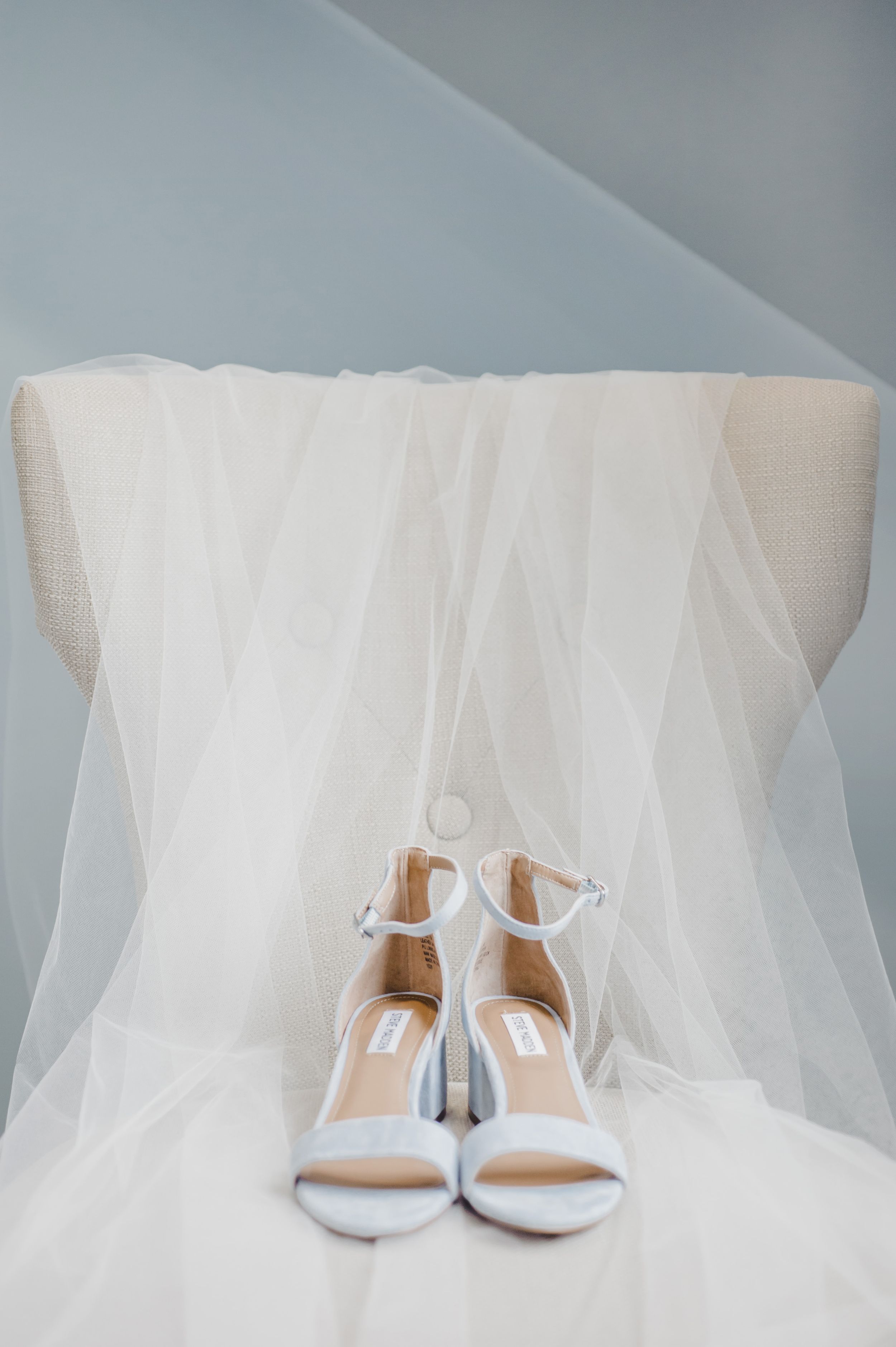 White wedding heels displayed elegantly with flowing tulle veil against a light background.