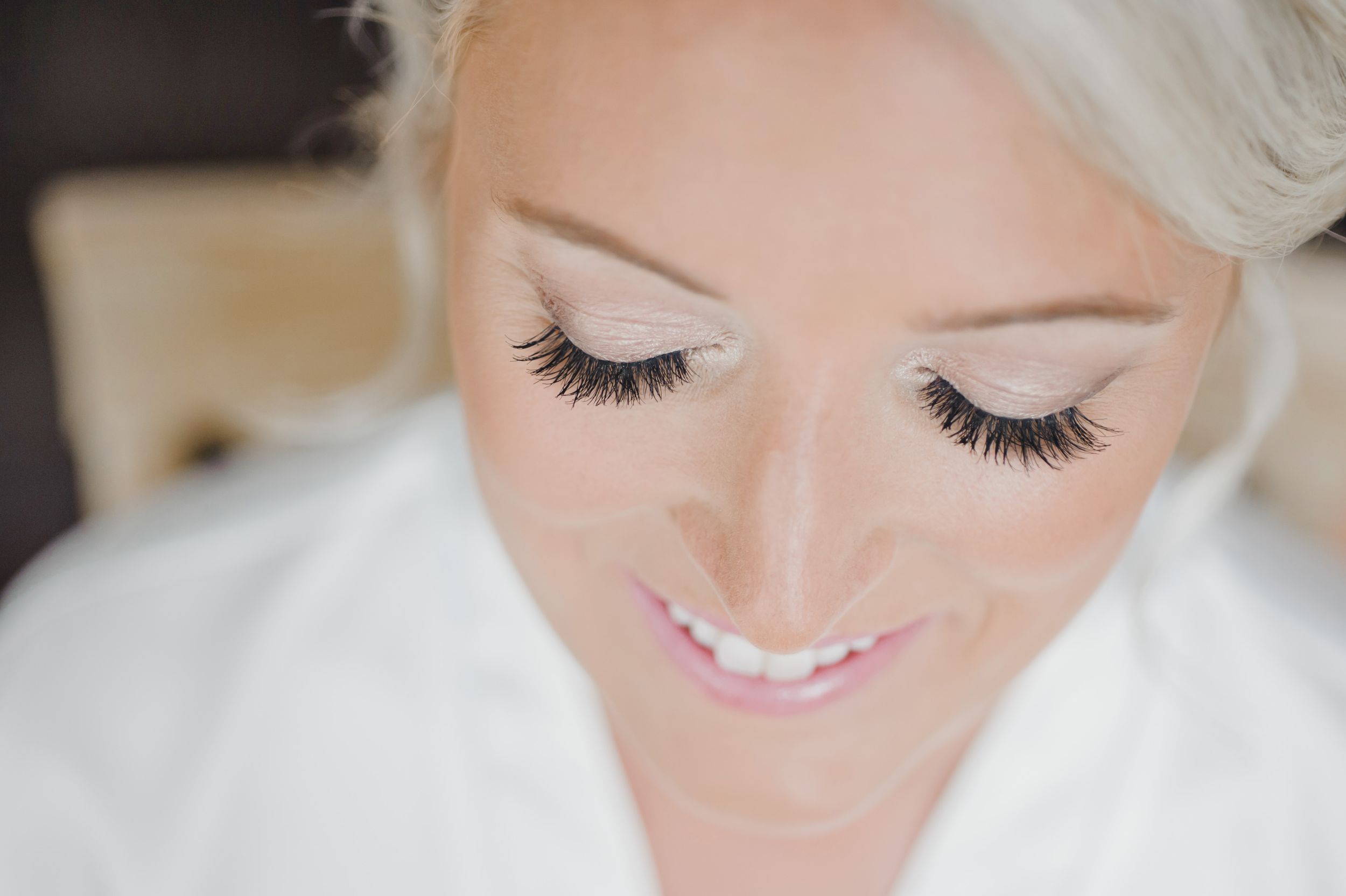 Close up beauty shot showing delicate makeup and long eyelashes against light background.