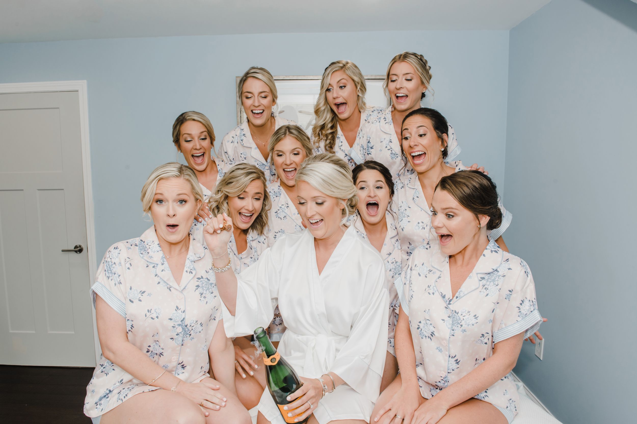 A festive group in matching floral robes celebrates with champagne during wedding morning preparations.