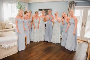 Bridesmaids wearing matching blue-gray dresses pose together in a sunlit room.