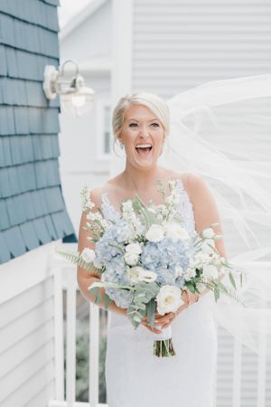 A bride holding a blue and white floral bouquet while her veil flows in the wind.