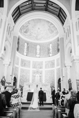 Black and white photo of a wedding ceremony in a grand cathedral with vaulted ceilings and religious artwork.