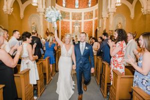 A joyful wedding recessional in a church aisle with guests applauding.
