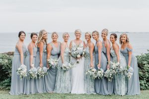 Wedding party in light blue dresses poses in line formation with ocean backdrop.