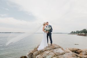 Elegant coastal wedding photo with couple standing on dramatic rocky overlook.