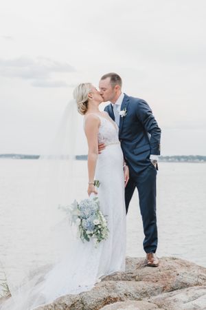 Intimate wedding moment captured on rocky coastal outcrop with ocean view.