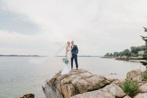 Wedding couple standing on coastal rocks overlooking the ocean in dreamy light.