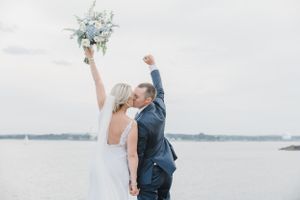 Newlyweds celebrating with raised arms against a waterfront backdrop.