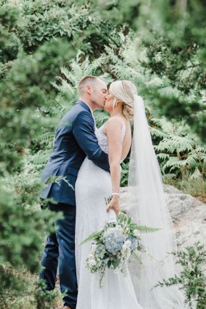 Romantic wedding portrait among lush green ferns with flowing white veil.