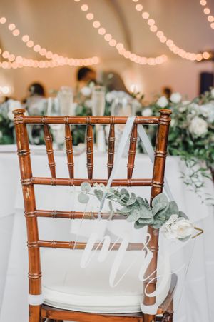 Elegant bamboo wedding chair decorated with white ribbon and eucalyptus under romantic string lights.