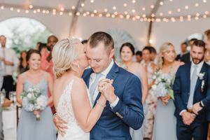 Intimate first dance under string lights with wedding party looking on.