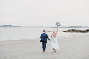 Wedding couple dancing and twirling on a serene beach with ocean views.