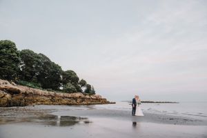Distant view of couple walking along rocky coastal beach during overcast day.