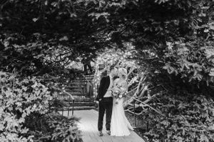 Black and white photo of couple standing on garden pathway surrounded by trees.
