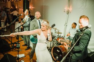 Live wedding band performs on stage while bride dances during reception celebration.