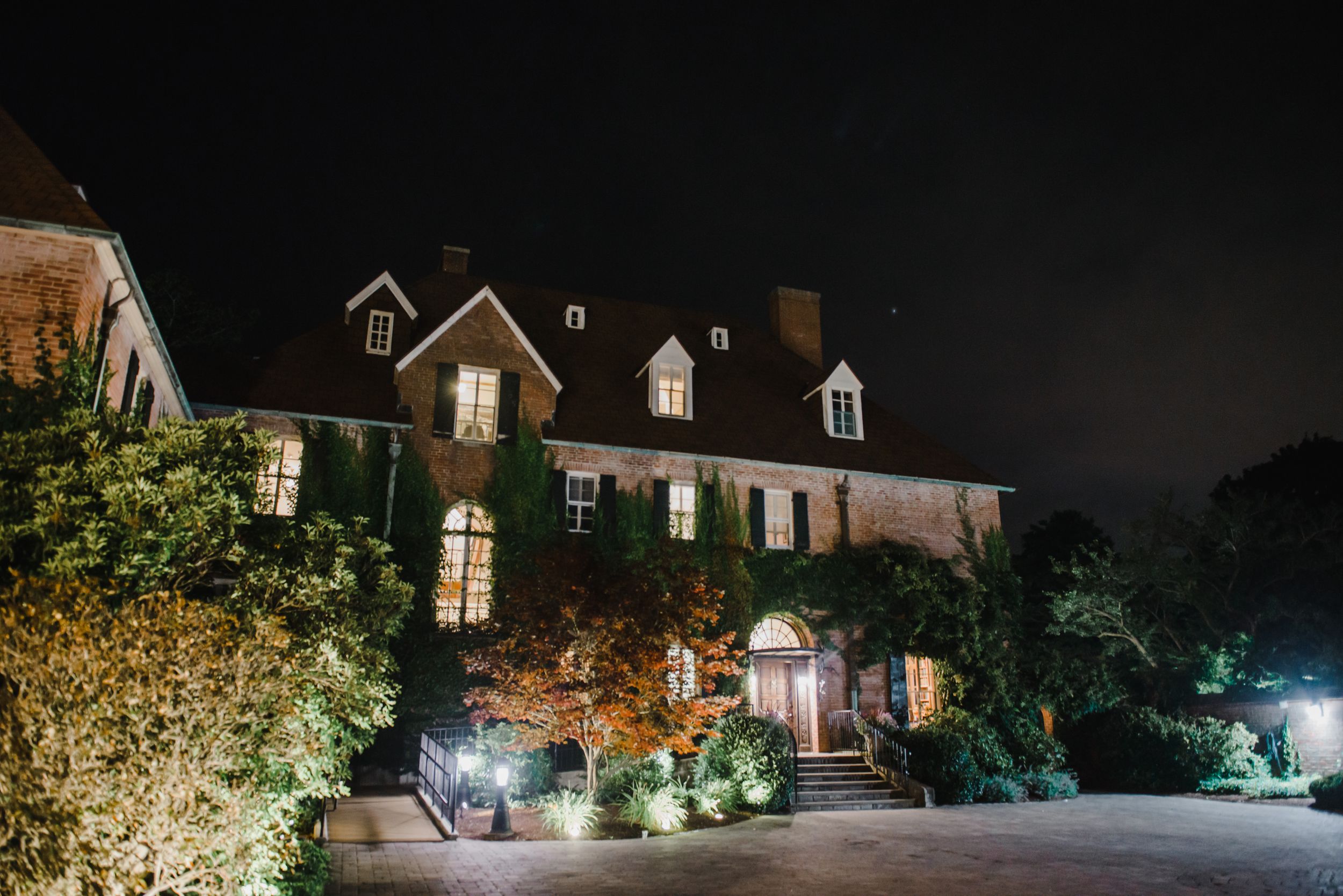 Elegant mansion illuminated at night with ambient landscape lighting and dormers.