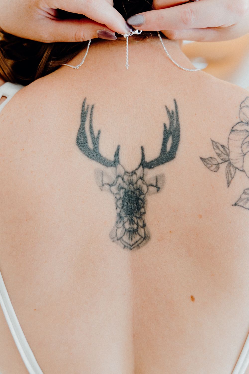 A geometric deer head tattoo of the bride in black ink on her upper back, captured by Apertured Media Auckland Wedding Photographer.