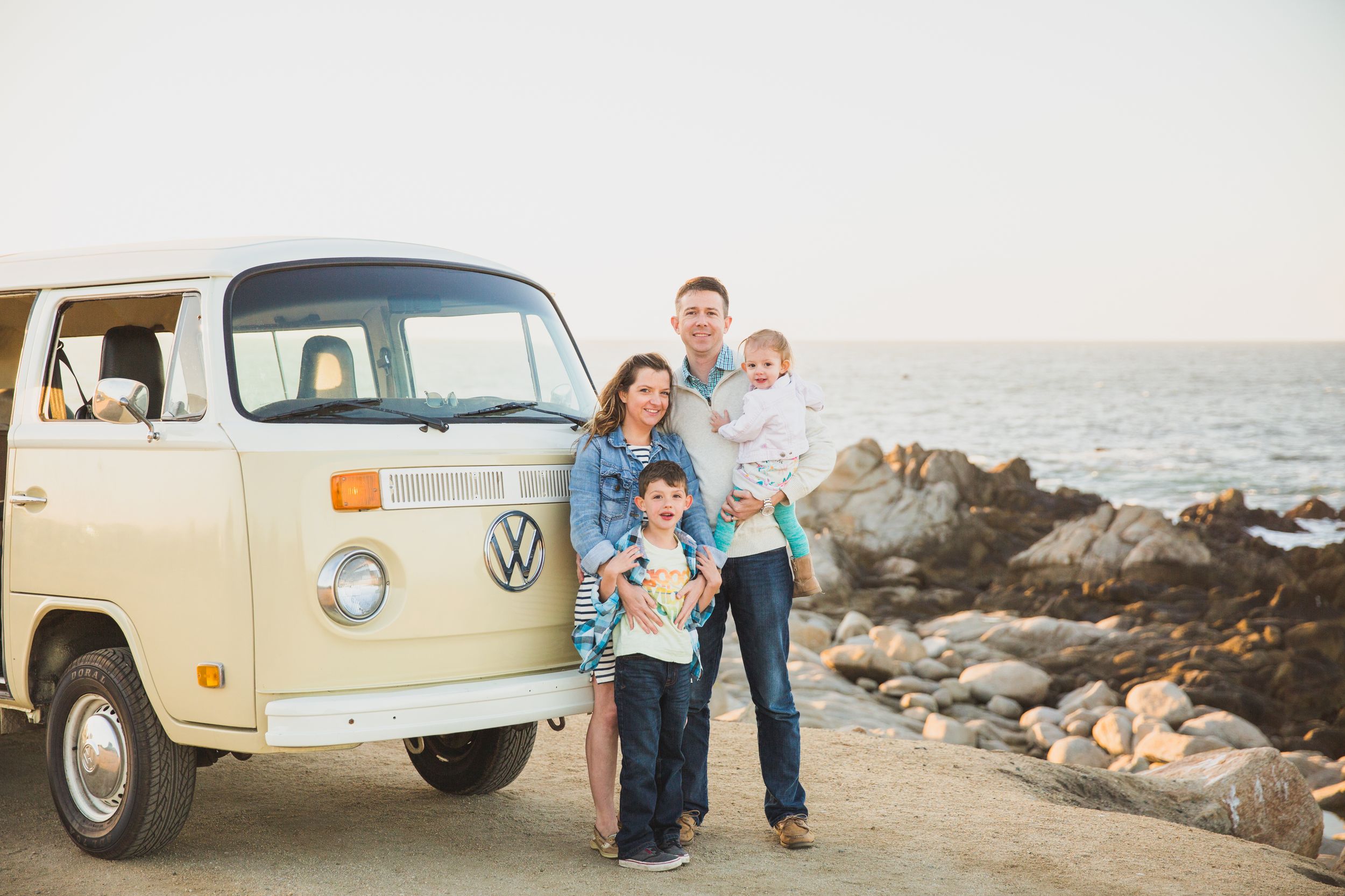 A classic cream-colored Volkswagen bus parked near a rocky beach at sunset at Asilomar in Pacific Grove.
