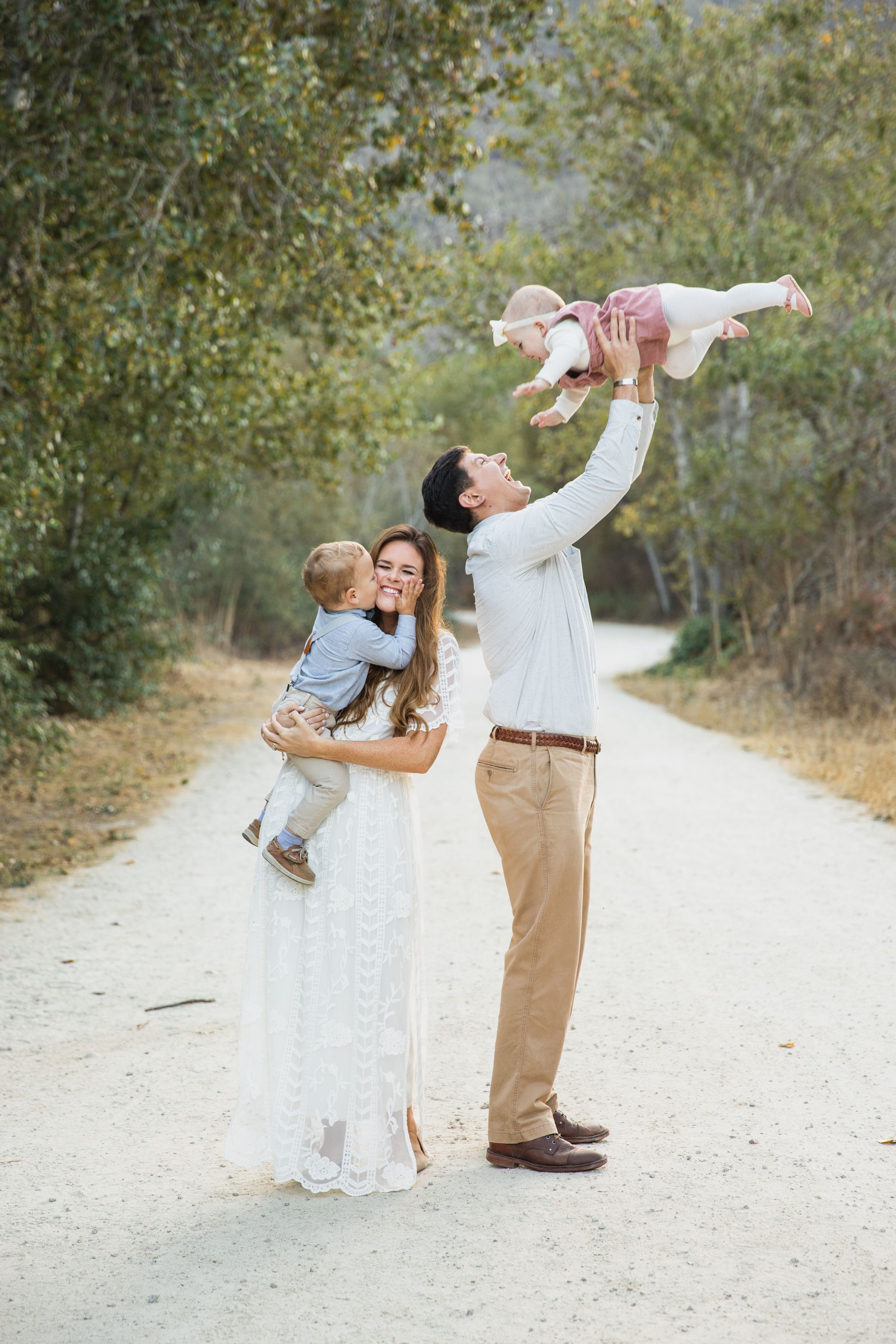 A family enjoys a playful moment together on a dirt path surrounded by trees in an outdoor nature setting at Garland Ranch in Carmel Valley.