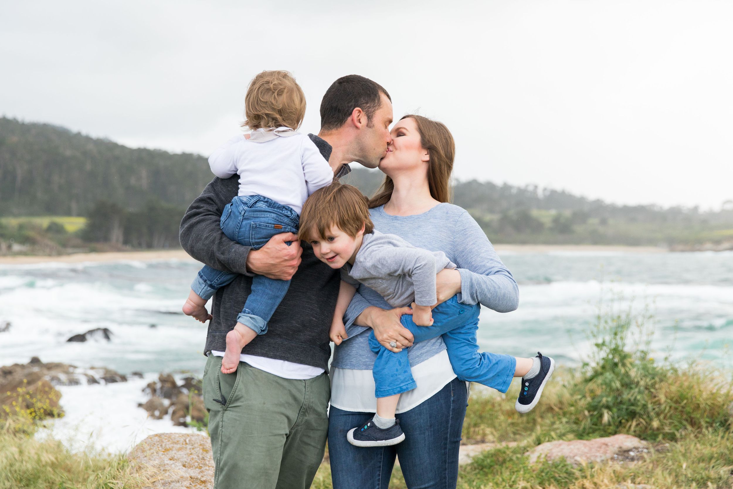 Family sharing tender moment together on coastal cliff overlooking ocean waves in Monterey, California.