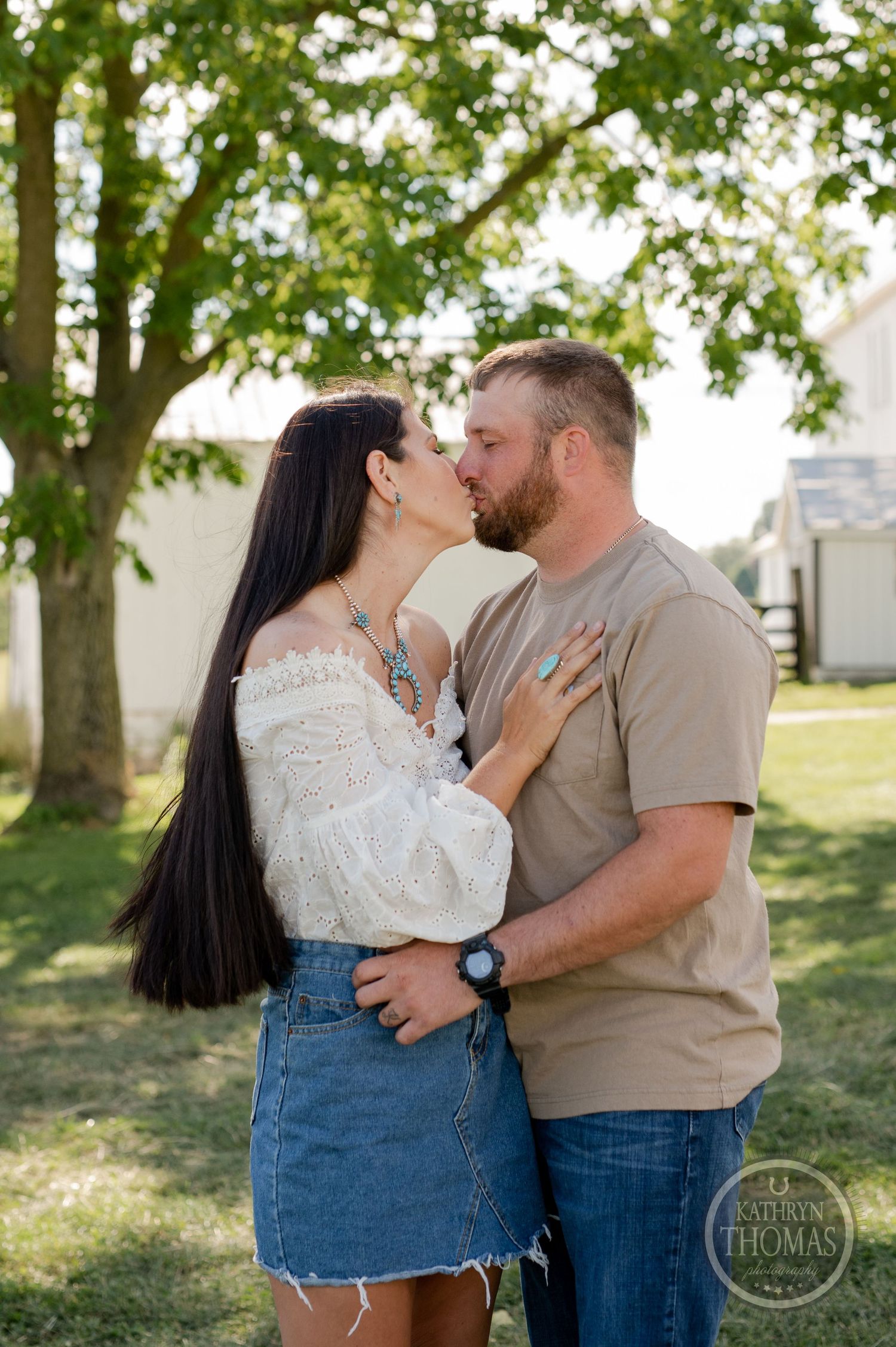 Romantic couple sharing intimate moment outdoors with trees and barn in background.