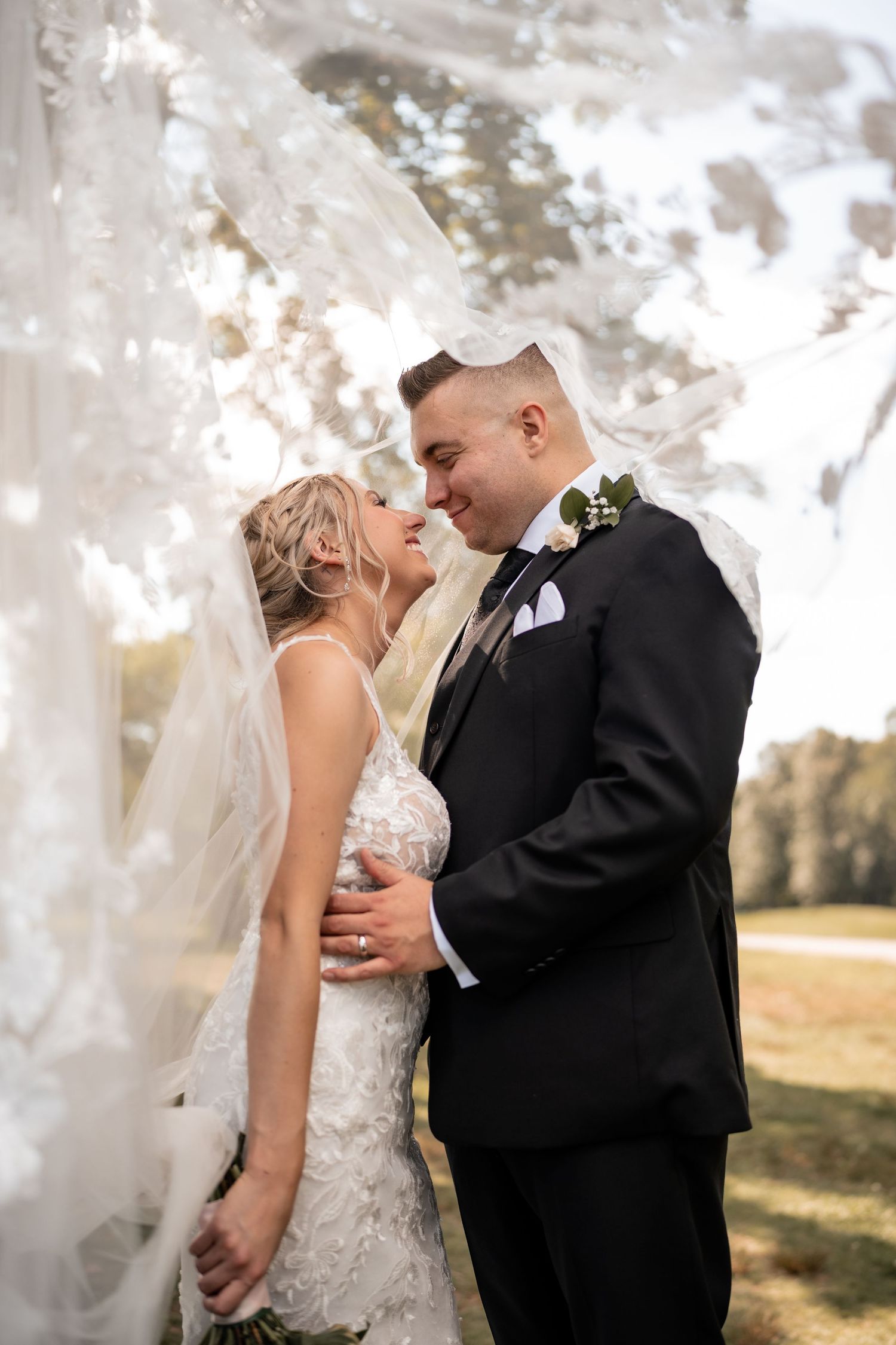 A tender wedding moment captured through delicate veil details in golden sunlight.