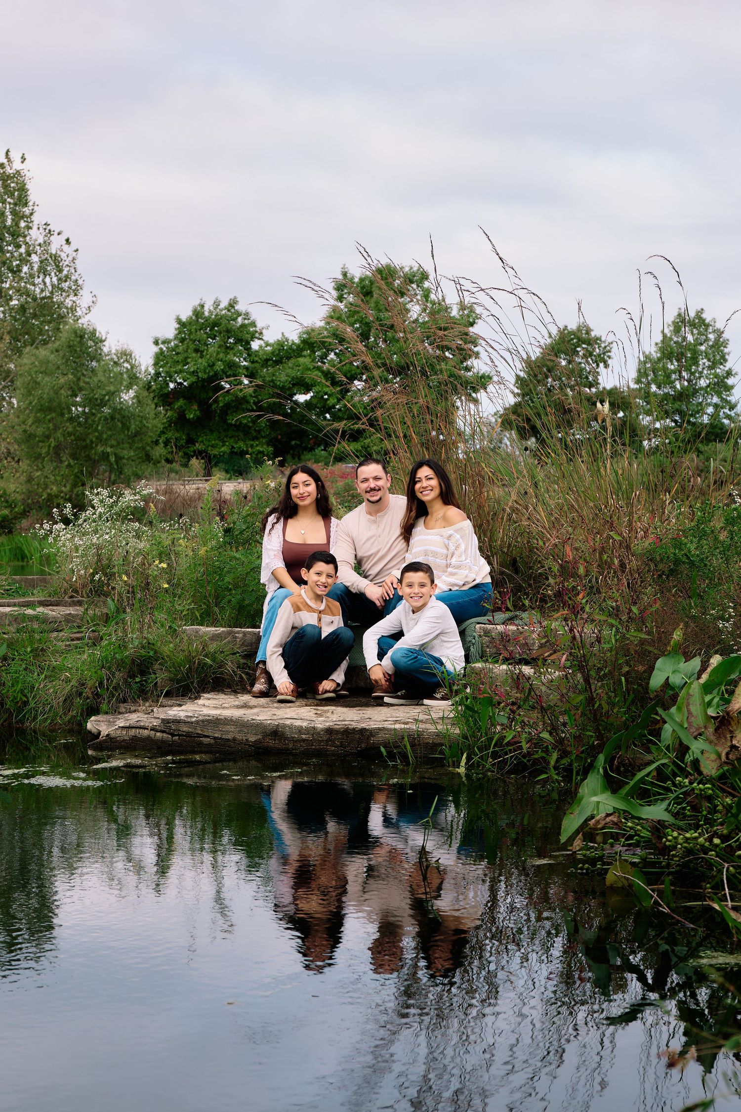 Family group sitting together on rocks by a reflective pond in a natural outdoor setting.