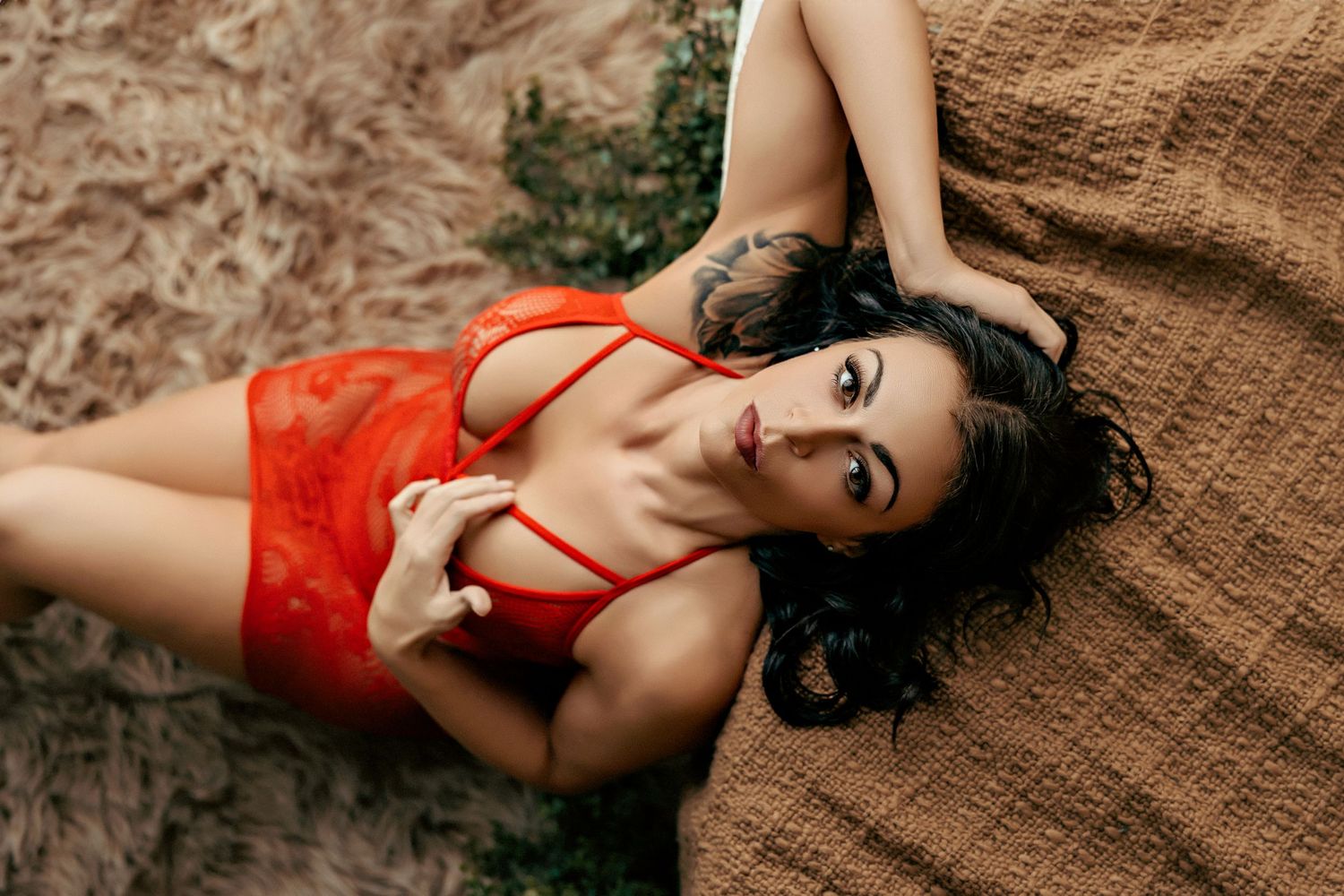 Model in red lingerie set poses elegantly on brown fabric during boudoir photo session.