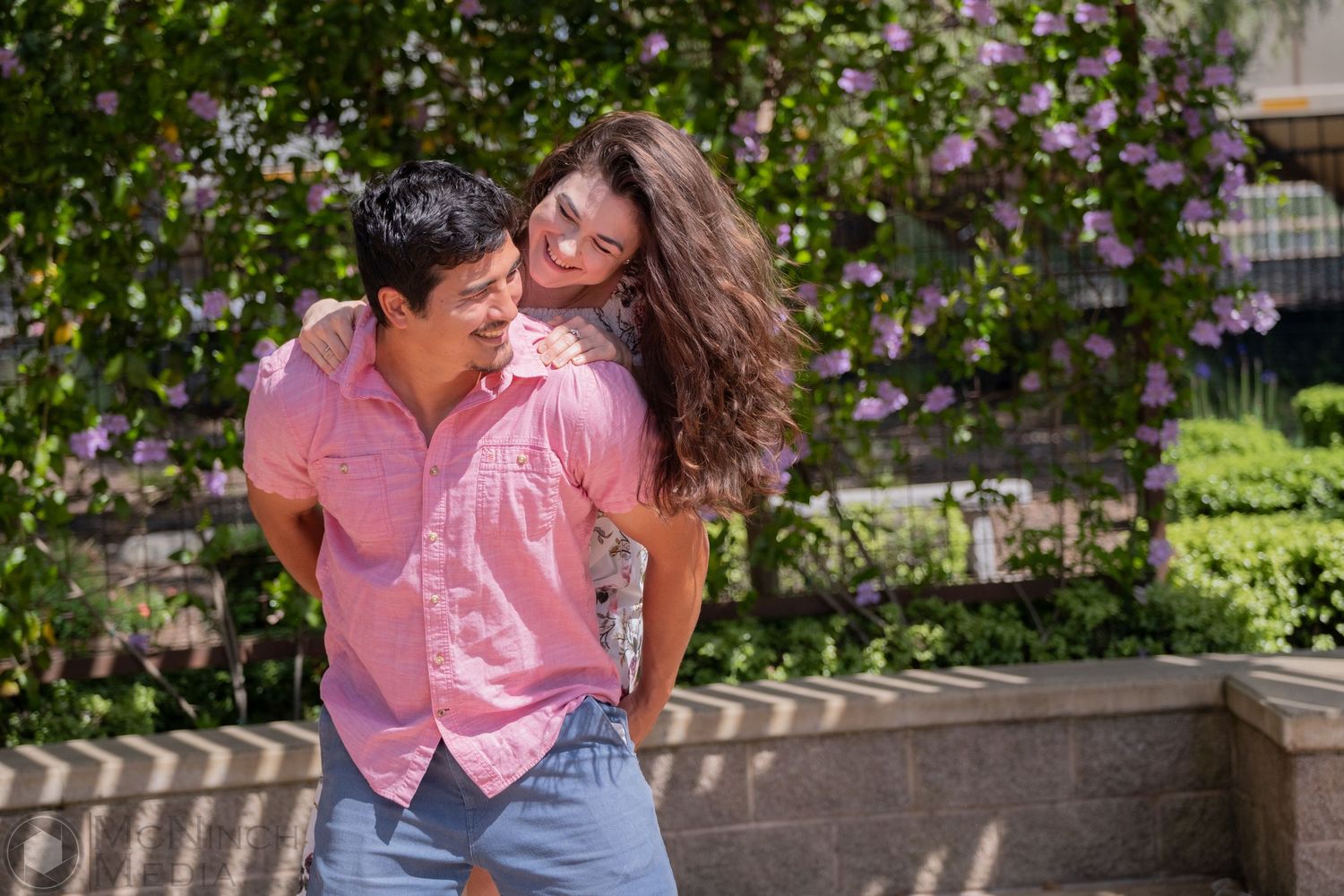 Playful couple laughing together against a blooming garden wall.
