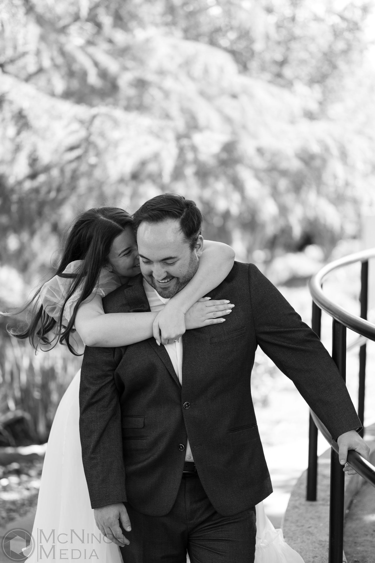 Candid black and white photo showing a joyful embrace on a garden pathway.